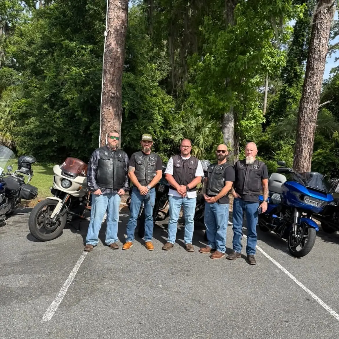 UNWORTHY MC members standing together with their motorcycles beneath the trees.