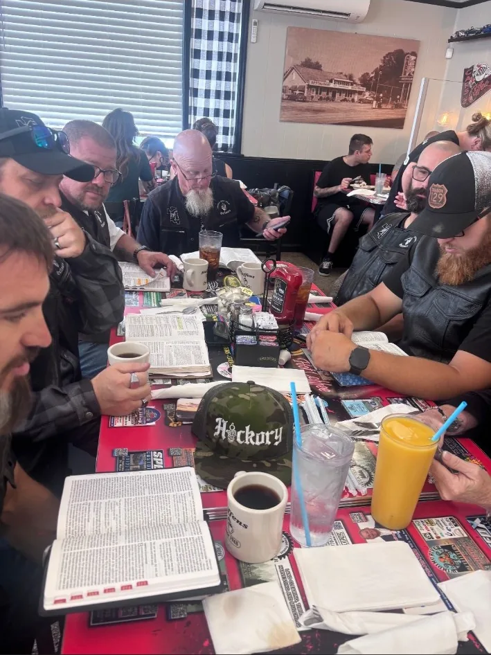 UNWORTHY MC members gathered around open Bibles at a restaurant table.